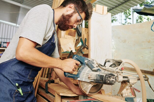 Premium Photo | Serious carpenter in apron and protective glasses ...