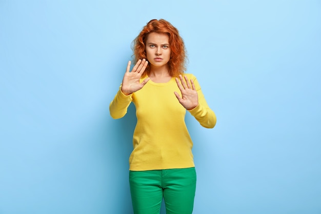 Free Photo Serious Discontent Woman Has Wavy Red Hair Shows Stop Gesture Keeps Palms Outstretched At Camera Refuses Something