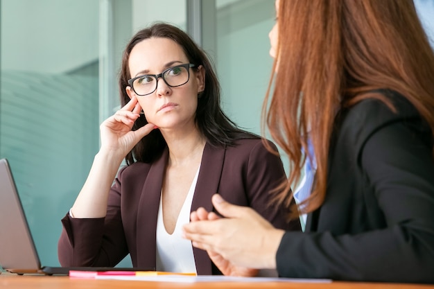 企業の会議で同僚に聞いて 眼鏡とオフィススーツを着ている深刻な女性専門家 無料の写真