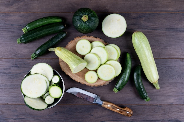 Set of knife and other zucchinis in a bowl and around and sliced zucchinis on a dark wooden table. flat lay. Free Photo