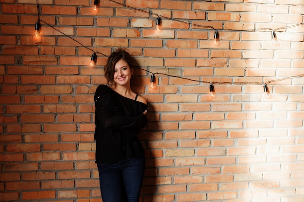 Sexy beautiful woman in black sweater and jeans standing near a retro red brick wall  Free Photo