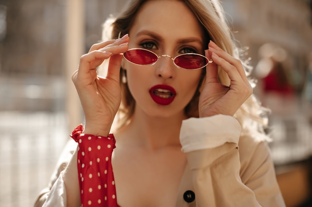 sexy-blonde-woman-with-red-lips-puts-colorful-sunglasses-attractive-curly-lady-beige-trench-coat-looks-into-camera-outdoors_197531-23192.jpg