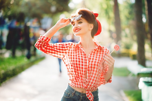 手でロリポップのセクシーなピンナップガールは 公園 レトロなアメリカンファッションで歩きます ピンナップスタイルで魅力的な女性 プレミアム写真