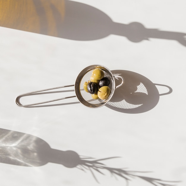 Free Photo | Shadow of strainer with organic olives on white background