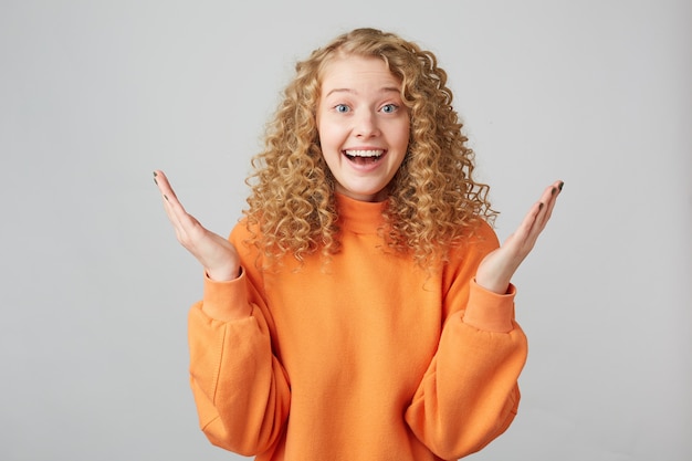 Free Photo Shocked Blonde Girl With Curly Hair And Blue Eyes Looking At The Front Holding Her Palms Up Isolated On White Wall