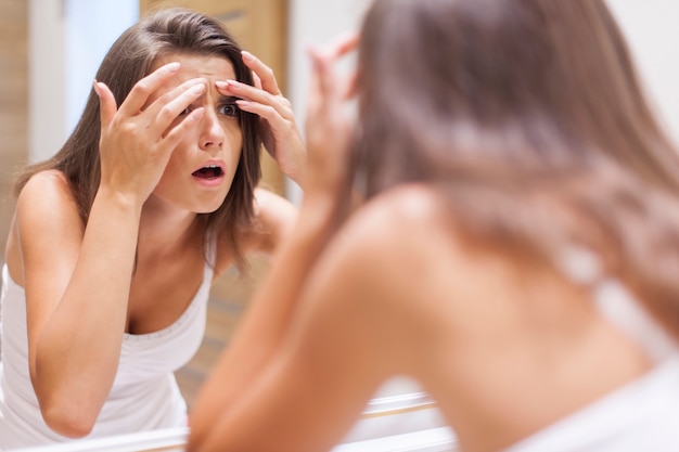 Shocked woman squeezing pimple in bathroom Free Photo