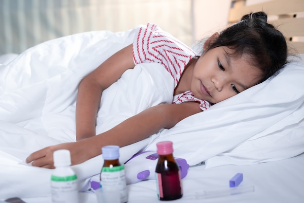 Premium Photo | Sick asian child girl is lying on bed and looking sadly on  medicine.
