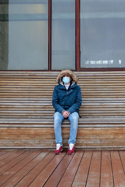 Premium Photo | Sick man with a hood sitting alone on bench, wearing  protective facial mask. coronavirus pandemic