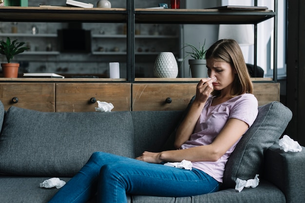 Sick woman sitting on sofa blowing her nose Free Photo