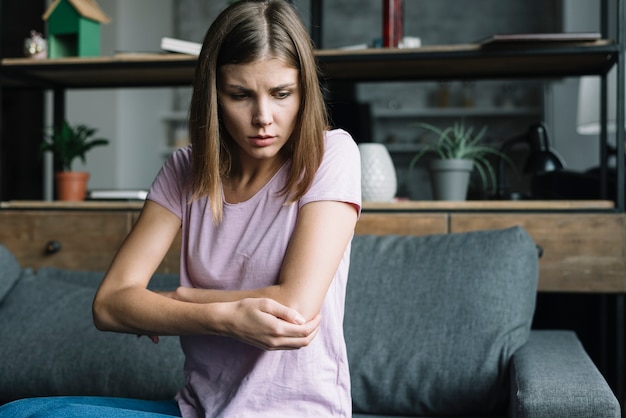 Sick woman sitting on sofa touching her elbow | Free Photo