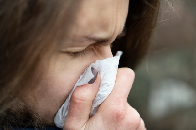 寒い日に路上で立っているハンカチで鼻をかむ病気の若い白人女性 プレミアム写真