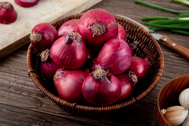 Side view of basket full of red onions on wooden background Free Photo
