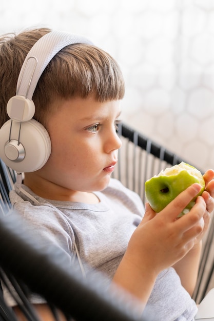 Side view boy with headphones eating apple | Free Photo