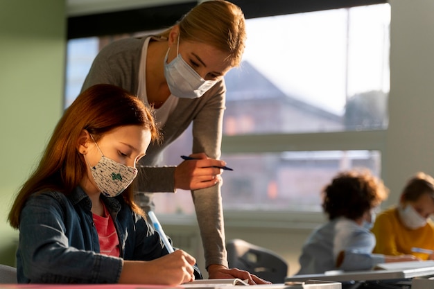 Side view of children learning in school with teacher during the pandemic Free Photo