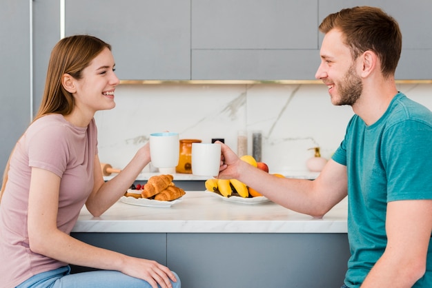 Free Photo | Side view of couple in the kitchen holding cups
