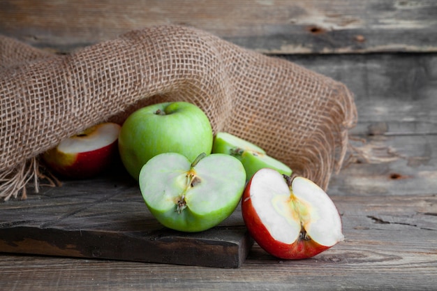 Free Photo Side View Green And Red Apples And Cut In A Half On Wood Cloth And Dark Wooden Background Horizontal