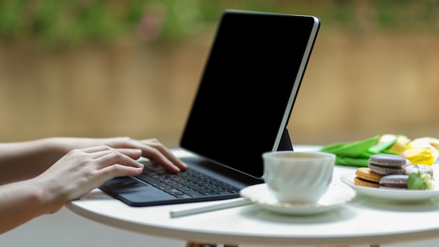 Premium Photo Side View Of Hand Typing On Tablet Keyboard On Coffee Table With Tae Cup And French Colourful Macarons