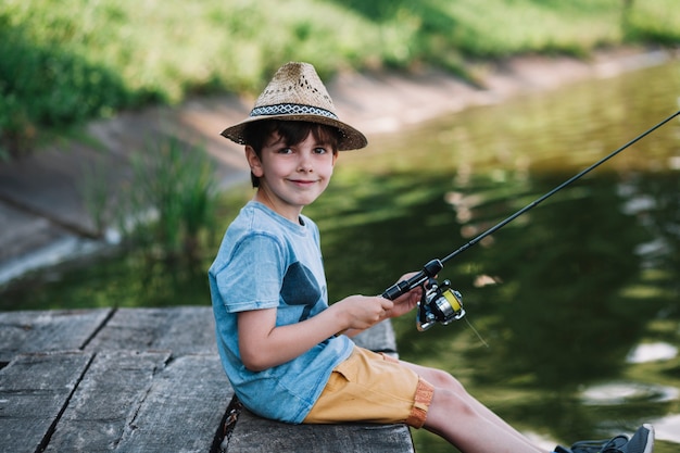 Side view of a happy boy wearing hat fishing on lake Photo | Free Download