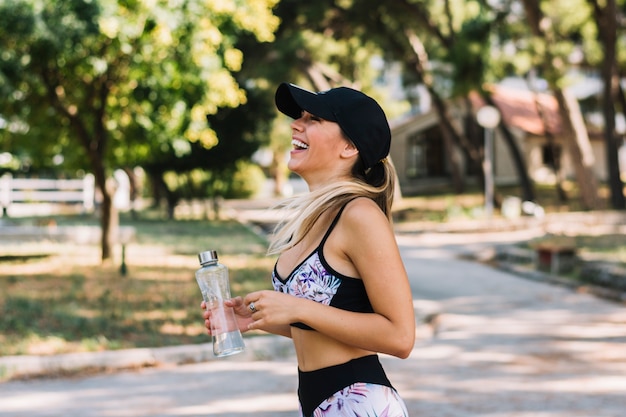 Side view of a happy young woman standing in the park holding water bottle Free Photo