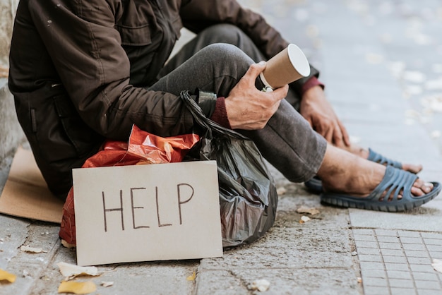 Free Photo | Side view of homeless man holding cup and help sign