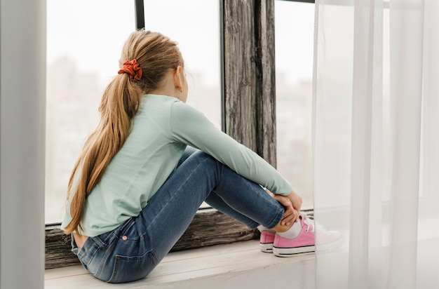 Free Photo - Side view little girl sitting on a window sill