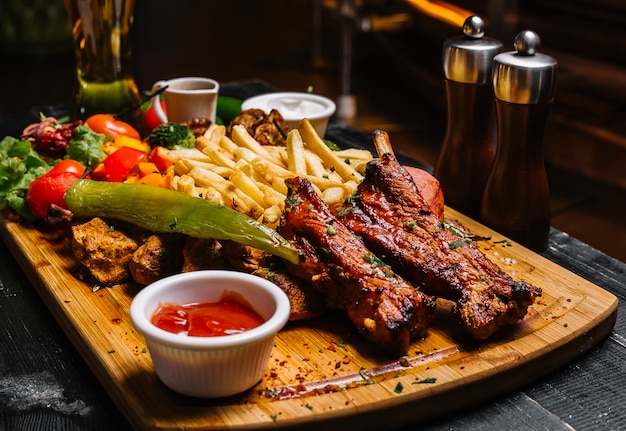 Side view mix of meat snacks with french fries grilled vegetables salad and sauces on the board Free Photo