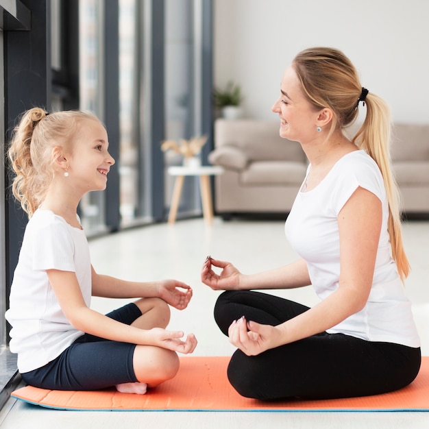 Free Photo | Side view of mother and daughter doing a yoga pose at home