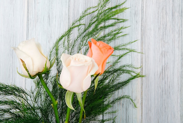 灰色の木製の背景にアスパラガスとピーチとクリーム色のバラの花束の側面図 無料の写真