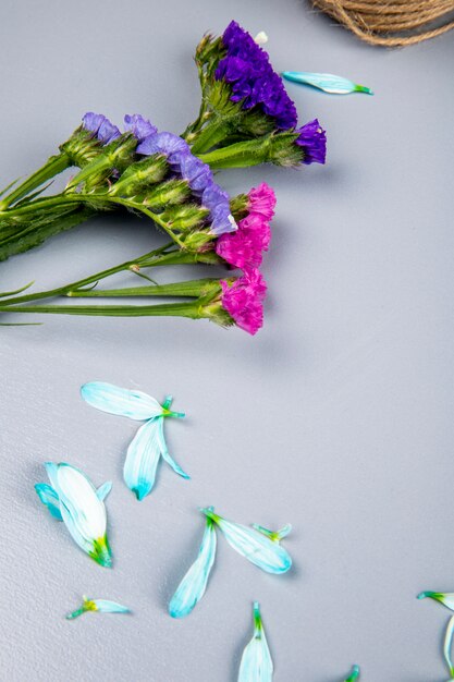 白いテーブルの上に散らばって花びらとピンクと紫のスターチスの花の側面図 無料の写真