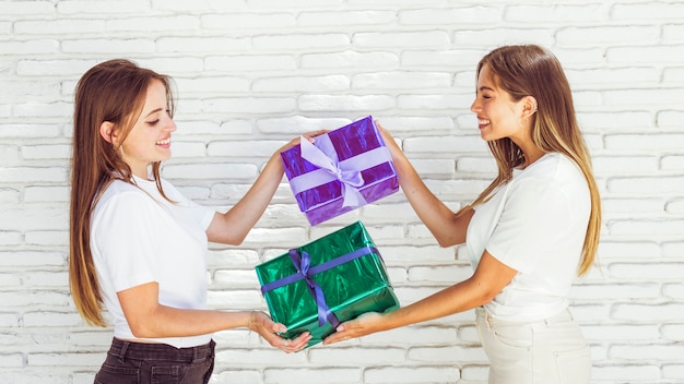 Side view of two happy female friends giving gift to each other Photo ...