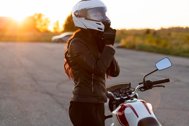 Free Photo | Side view of woman taking off her helmet next to motorcycle