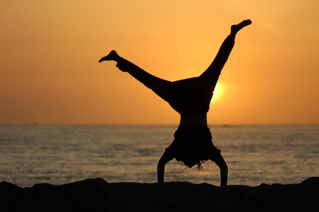 Silhouette of a female doing a cartwheel with a blurred sea and a clear ...