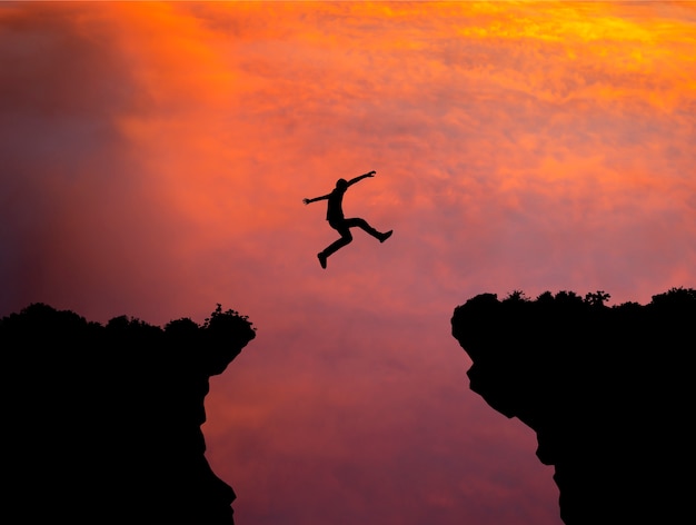 Premium Photo | Silhouette Of Man Jumping Over Cliff On Sunset Background