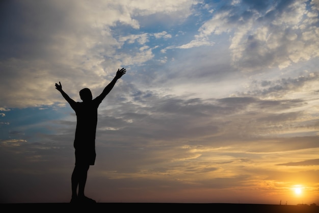 Premium Photo | Silhouette of a man with hands raised in the sunset.