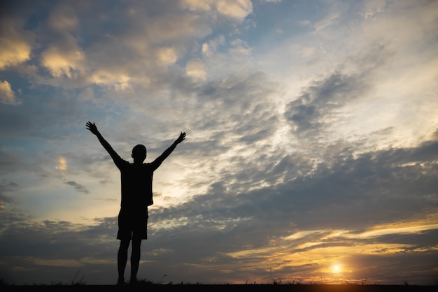 Premium Photo | Silhouette of a man with hands raised in the sunset.