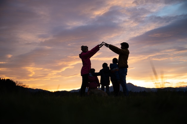 美しい夕方の空の下で 両親が 3 人の子供と犬の上に腕を組んで家を建てる家族のシルエット プレミアム写真