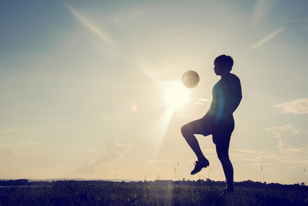 夕日の背景にサッカーボールを持つサッカー選手のシルエット プレミアム写真