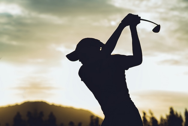 若い女性ゴルフプレーヤーのシルエットが抜本的なヒットし ゴルフスイングを行うゴルフコースを維持 彼女はリラックス時間の運動を行う プレミアム写真