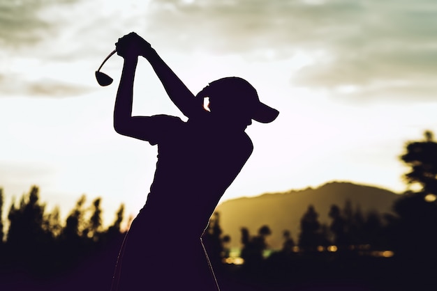 若い女性ゴルフプレーヤーのシルエットが抜本的なヒットし ゴルフスイングを行うゴルフコースを維持 プレミアム写真