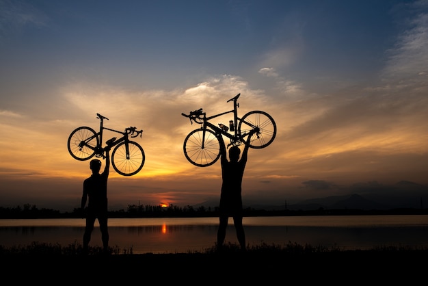 朝 頭上に自転車を持っているシルエット2ロードバイクサイクリストの男 プレミアム写真