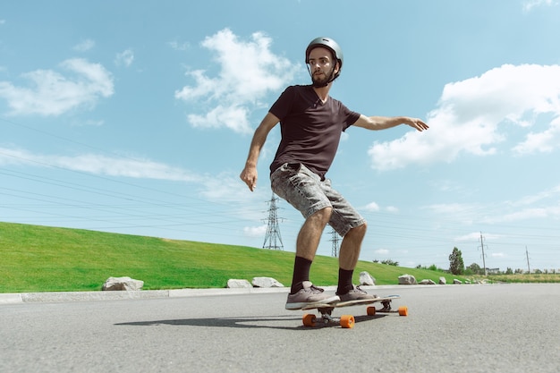 Skateboarder doing a trick at the city's street in sunny day. young man in equipment riding and longboarding near by meadow in action. concept of leisure activity, sport, extreme, hobby and motion. Free Photo