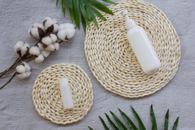 Premium Photo | Skin care mock up bottle on wicker pad with cotton flowers and palm leaves