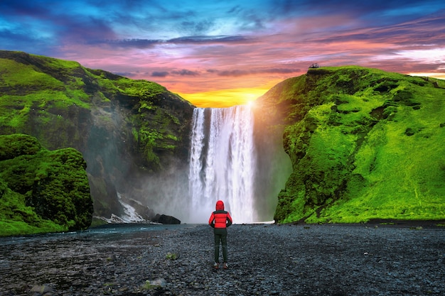 アイスランドのスコゥガフォスの滝 赤いジャケットを着た男がスコゥガフォスの滝を見ています 無料の写真