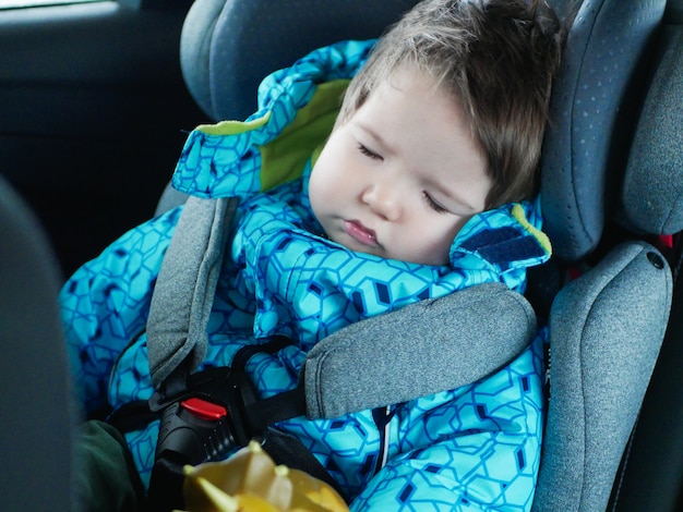 眠っている赤ちゃんは車の座席に乗ります 車で幸せな赤ちゃんに乗る 子供の安全 チャイルドシートの車で寝ているかわいい男の子 プレミアム写真
