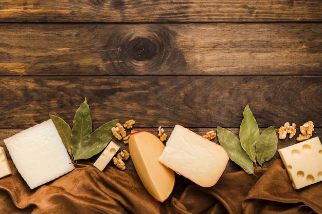 Slice of cheese; bay leaves and walnut arrange at bottom of the wooden background with silk material textile Free Photo