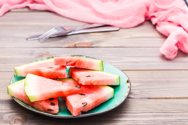 Sliced watermelon on a ceramic plate, cutlery and napkin on a wooden table Premium Photo