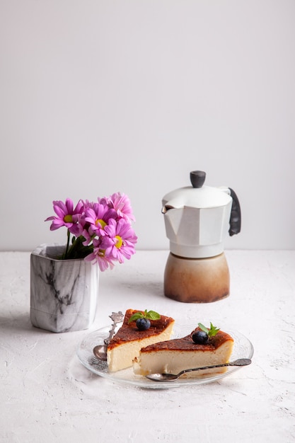 ブルーベリーとミントの葉 間欠泉のコーヒーメーカー 明るい背景の花瓶にライラックの花と自家製バスクの焦げたチーズケーキのスライス プレミアム写真