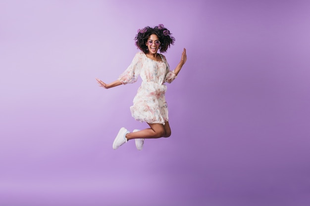 ジャンプして笑っている白いスニーカーのスリムなアフリカの女性 気さくな黒人少女が踊る室内写真 無料の写真