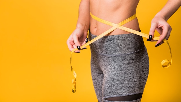 Slim lady in sportswear measuring waist by tape Free Photo