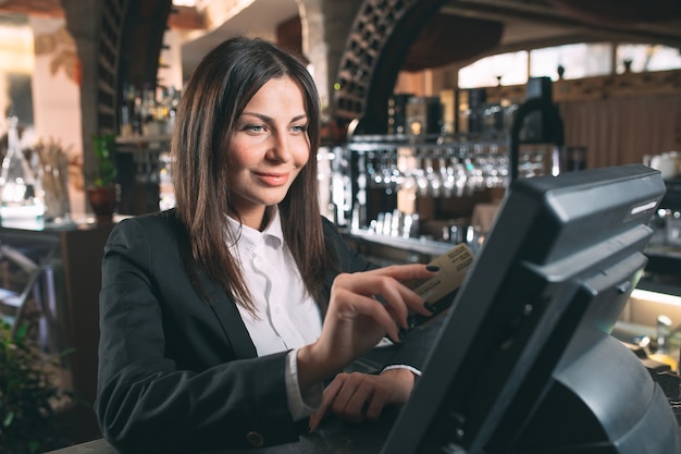 Small business, people and service concept - happy woman or waiter or manager in apron at counter with cashbox working at bar or coffee shop Premium Photo